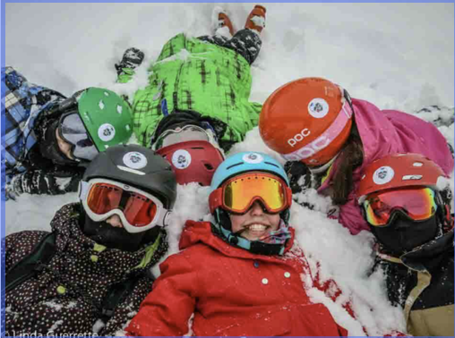Children wearing helmets and goggles lying together in the snow